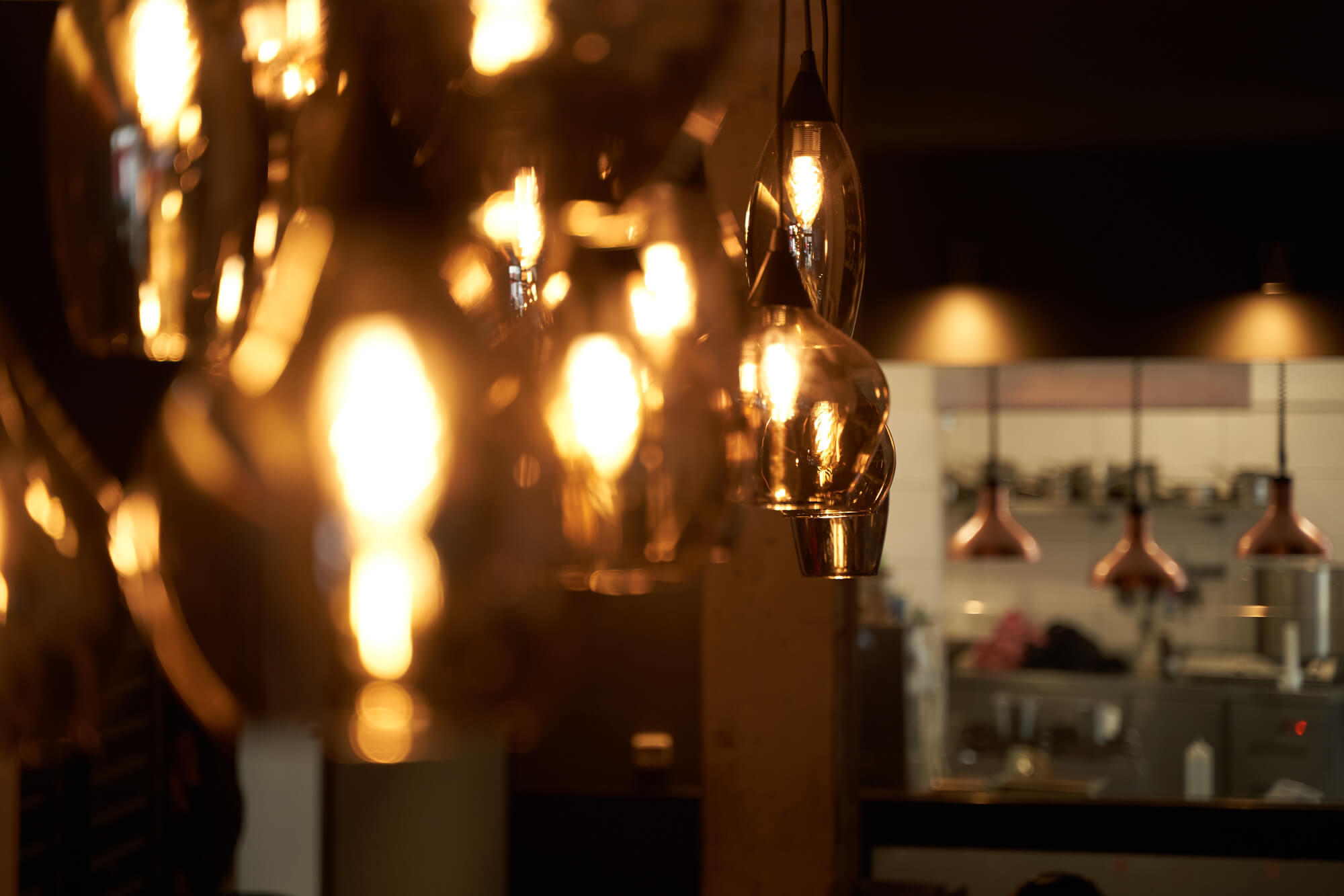 Nahaufnahme der schönen Innenraumlampen im dario& Restaurant mit Blick auf die Küche im Hintergrund.