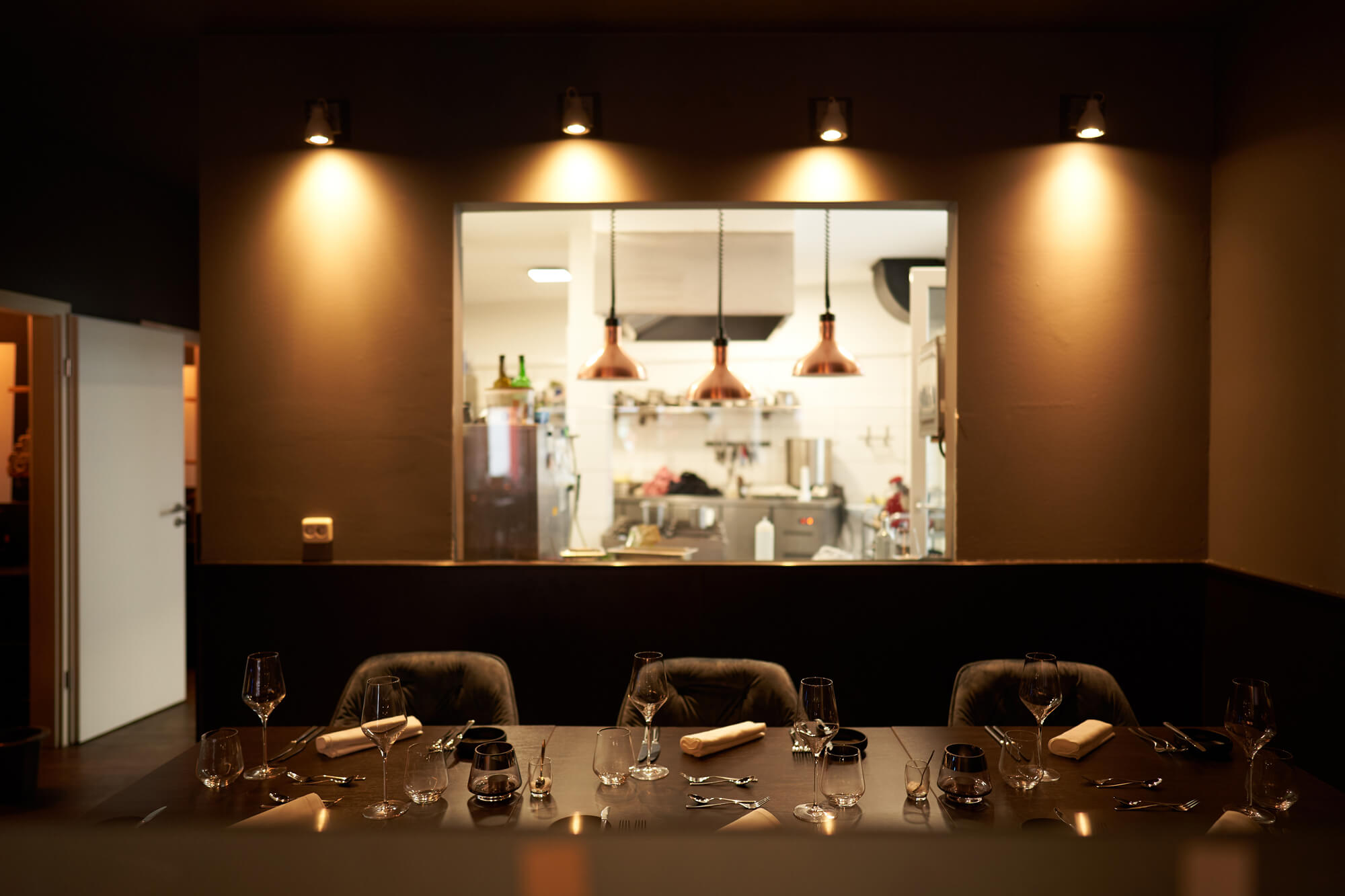Ansicht eines Tisches für 6 Personen im dario& Restaurant. Im Hintergrund ist die Küche durch eine Scheibe zu sehen.